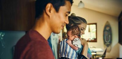 En mann og en dame står inne i en stue og tar vare på en baby