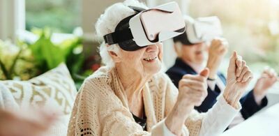 En eldre dame sitter med VR-headset og smiler. Foto