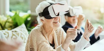 En eldre dame sitter med VR-headset og smiler. Foto