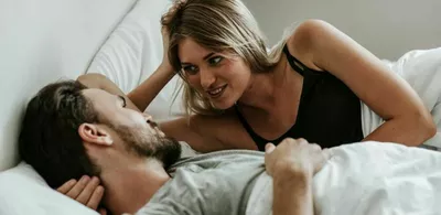 Et par ligger i en seng og ser smilende på hverandre. Foto