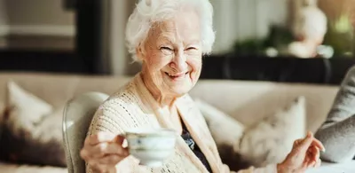 En eldre dame skåler med en kaffekopp. Foto