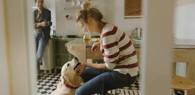 En dame koser med en hund, en mann står i bakgrunnen. Foto