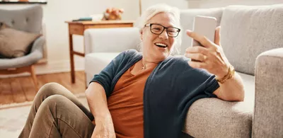 En dame sitter på gulvet og lener seg til en sofa mens hun ser på telefonen sin. Foto