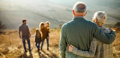 Et eldre ektepar står i vakker natur og ser på resten av familien sin