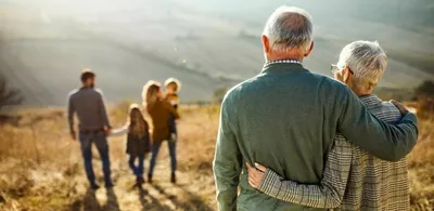 Et eldre ektepar står i vakker natur og ser på resten av familien sin