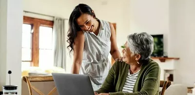 En dame står overfor en eldre dame som ser på en laptop. Foto