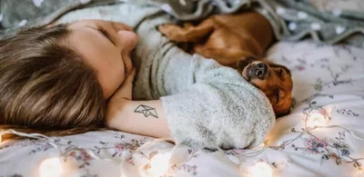 En dame ligger i en seng sammen med en hund. Foto