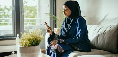 En dame sitter i en sofa og ser på telefonen sin. Foto