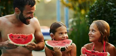 En mann står med to barn og spiser vannmelon. Foto
