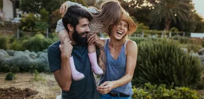 En mor, en far og en datter smiler og tuller. Datteren sitter på skulderene til far. Foto