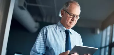 En mann står og ser ned på en Ipad. Foto
