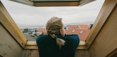 En dame lener seg til en vinduskarm og ser ut. Foto
