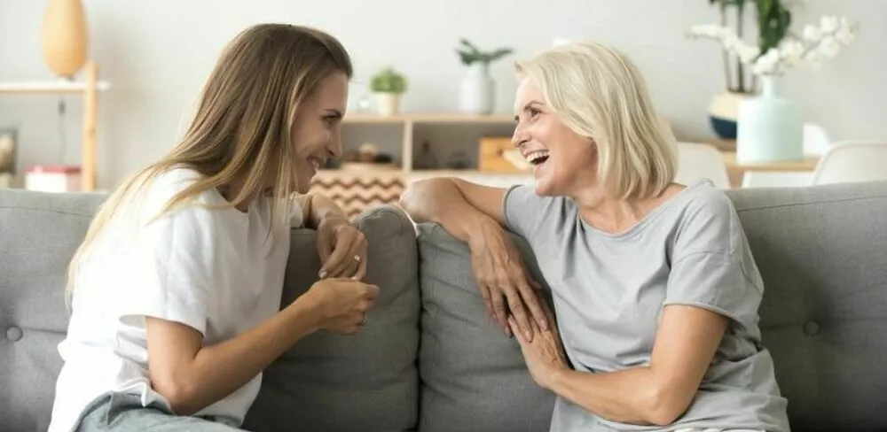 To damer sitter i en sofa og ser på hverandre og ler. Foto